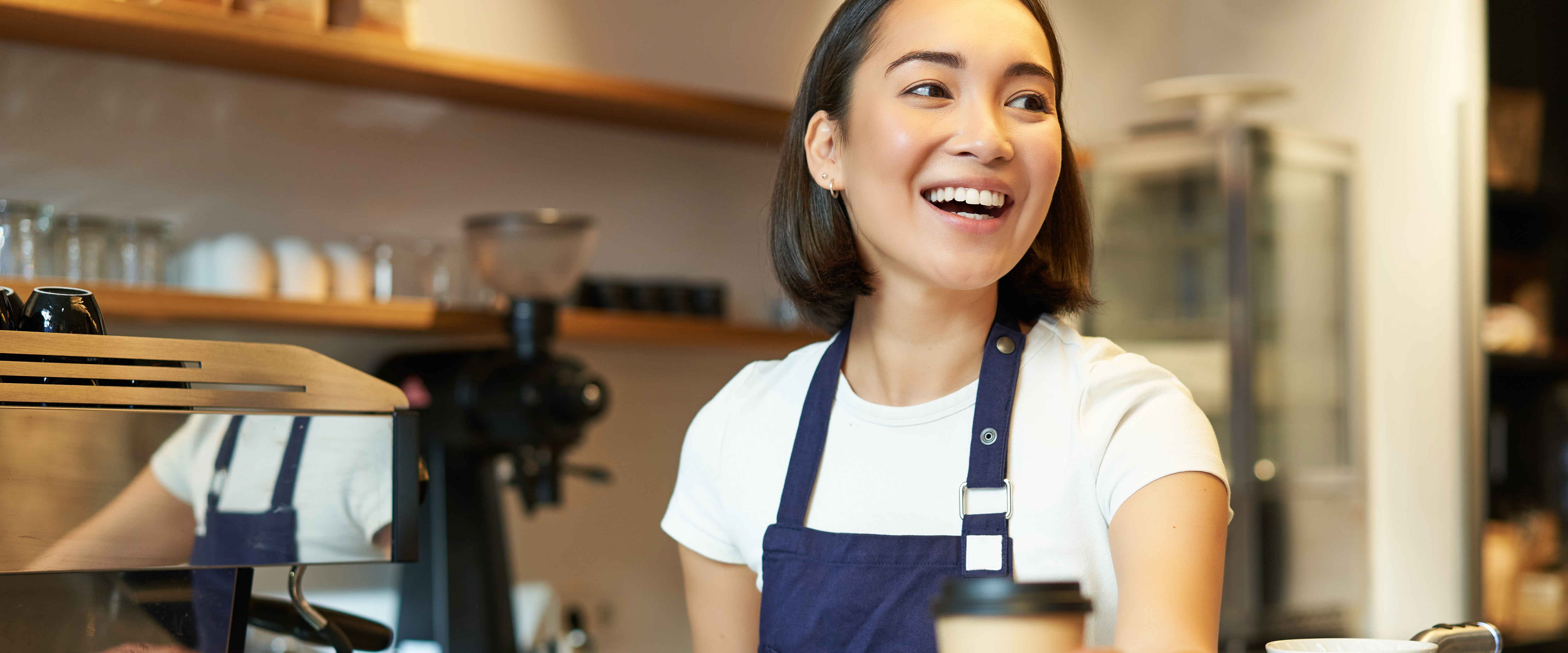 Smiling asian barista girl giving takeaway coffee cup prepare takeout order guest cafe wearing copy